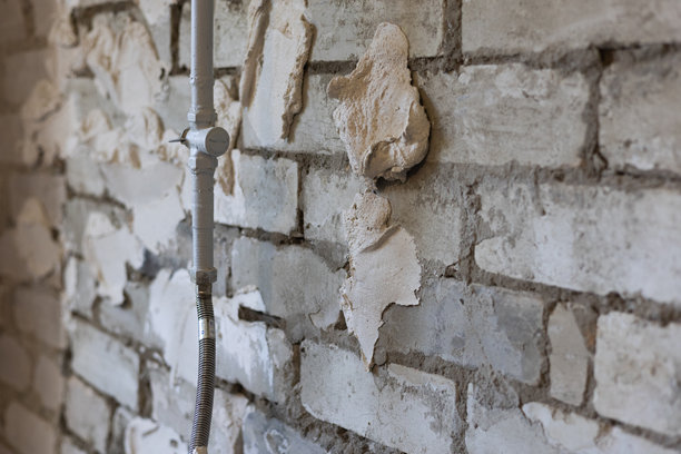 未完工的砖墙，带有白色腻子修补处和一个带柔性连接件的垂直管道，展示了翻新进度、纹理表面以及为油漆或抹灰所做的准备工作。图片下载