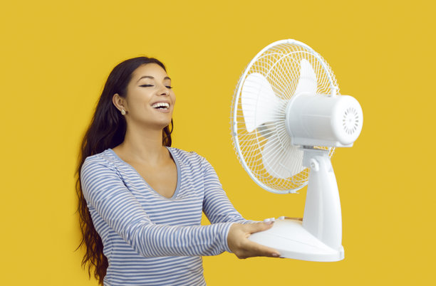 一名快乐的女子在黄色背景下享受电风扇吹来的风图片下载