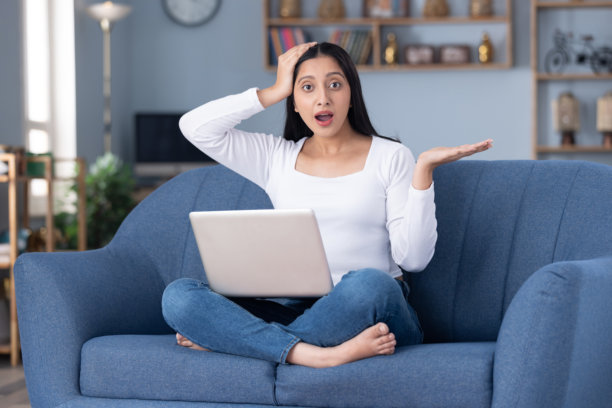 身穿现代服装的漂亮年轻女孩在家中坐在沙发上使用笔记本电脑的图片素材图片下载