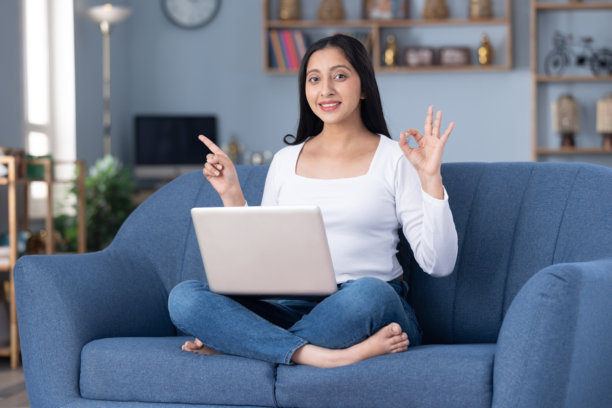 身穿时尚服装的漂亮年轻女孩在家中沙发上使用笔记本电脑的图片图片下载