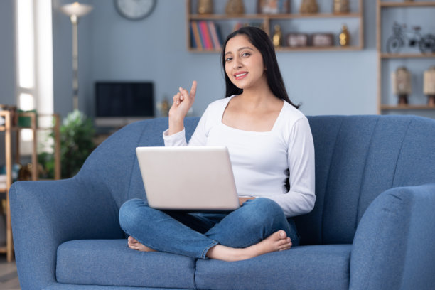 穿着时尚的漂亮年轻女孩在家中沙发上使用笔记本电脑的图片素材图片下载