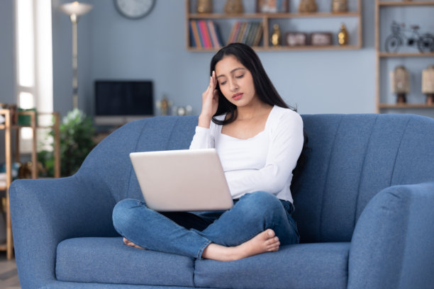 穿着时尚的漂亮年轻女子在家中沙发上使用笔记本电脑的图片素材图片下载