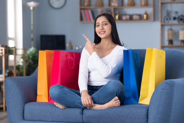 一位漂亮的年轻女孩提着购物袋坐在家中沙发上的照片素材图片下载