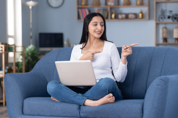 穿着时尚的年轻漂亮女孩在家坐在沙发上使用笔记本电脑的图片图片下载