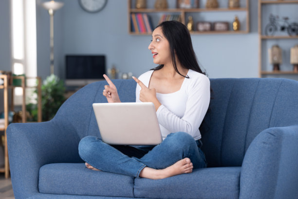 身穿现代服装的漂亮年轻女孩在家中沙发上使用笔记本电脑的图片素材图片下载