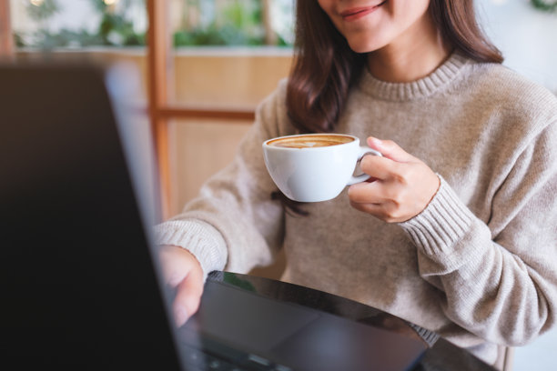 近距离拍摄一名女子在咖啡馆使用笔记本电脑工作并喝咖啡的特写照片图片下载