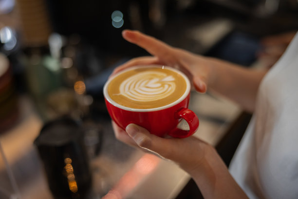女咖啡师手持拉花艺术心形图案的拿铁咖啡杯图片下载