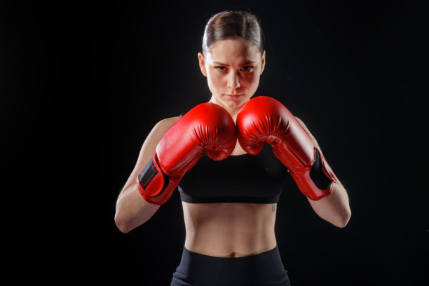 身着红色拳击手套的女性拳击手摆出防守姿势，黑色背景，留有复制空间图片下载