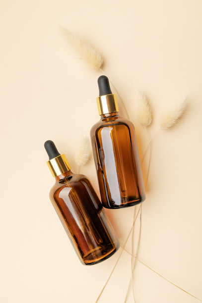 化妆品模型。琥珀棕色玻璃瓶配滴管和干花穗，背景为米色。美容和面部护理概念，精华，精油。天然化妆品包装设计图片下载