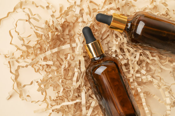 化妆品模型。琥珀棕色玻璃滴管瓶，置于米色背景上的手工切割纸上。美容和面部护理概念俯视。天然化妆品包装设计、精华、精油图片下载