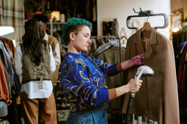 年轻白人女性在复古服装店里用蒸汽熨斗熨烫二手夹克图片下载