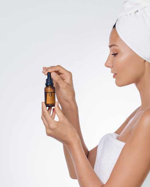 女性使用毛巾的个人美妆照，手持护肤精华瓶图片下载