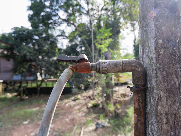 葱郁花园里的复古生锈水龙头，固定在混凝土柱上。图片下载