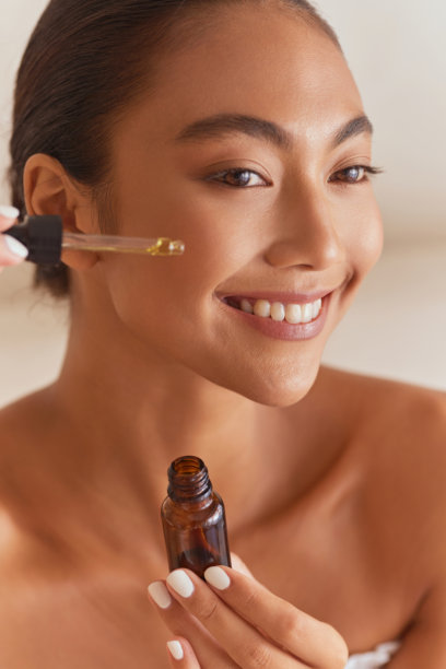 微笑的女性用滴管瓶涂抹面部精华图片下载