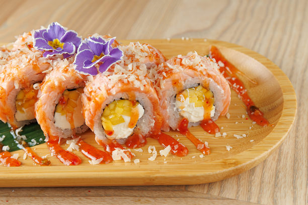 木盘上摆放着寿司卷，内馅为鸡蛋和芝士，并用蟹肉和鲜花装饰图片下载