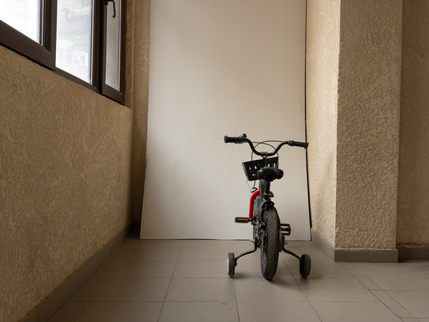 室内黑色儿童自行车的后视图，带有辅助轮。带篮子和稳定器的自行车在阳台上。白色背景上有复制空间。图片下载