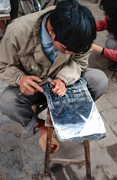 1995年3月18日，越南河内，一位越南男子蹲着，手持锤子和凿子在墓碑上工作的历史彩色照片图片下载