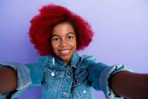 染着红发的年轻女孩穿着牛仔夹克，在紫色背景前自拍，这是一张有趣的时尚生活方式的图库照片图片下载