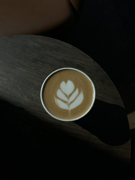 一杯精心制作的拿铁，浓郁的意式浓缩咖啡上覆盖着绵密的奶泡拉花。这张图片完美捕捉了经典咖啡馆体验的温馨与诱人之处，非常适合与咖啡相关的项目。图片下载