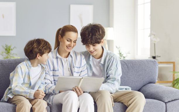 慈爱的母亲，一位关怀的女性，与年幼和青少年儿子一起观看相册中的照片图片下载