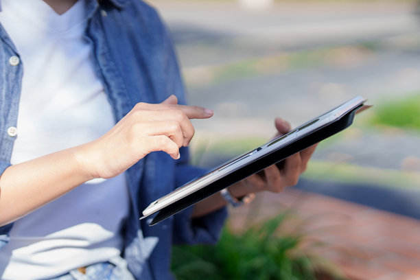 亚洲女性在户外公园使用平板电脑进行在线购物，平板电脑是电子商务、浏览网页、社交媒体的数字设备，手触碰屏幕，使用移动支付技术。图片下载