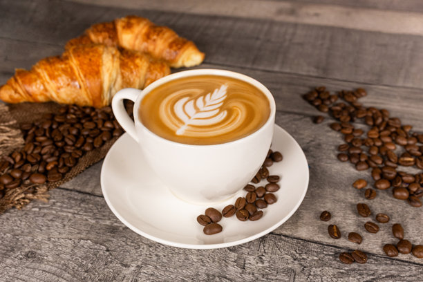 木质背景上的卡布奇诺咖啡，带有拉花艺术、羊角面包和咖啡豆。图片下载