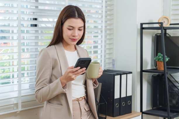 亚洲女员工在现代办公室工作空间使用智能手机喝咖啡，代表着当代女商人的生活方式、通讯技术、生产力和职业生涯图片下载