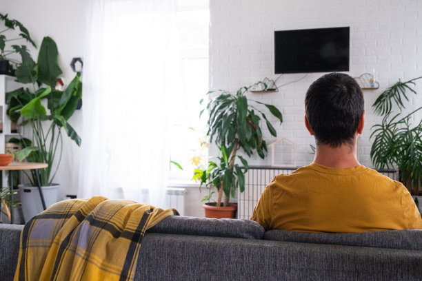 男人在家中白色内饰的沙发上观看电视，黑色屏幕模拟。居家娱乐，休闲图片下载