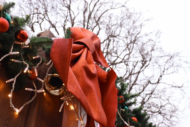 圣诞花环，饰有红色蝴蝶结、彩球和花饰，背景为冬季树枝和多云的天空图片下载