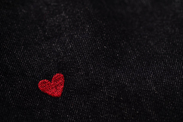 黑色牛仔布纹理特写，带有小小的红色心形刺绣，极简爱意概念，富有情感的时尚背景，留有复制空间，非常适合浪漫、生活方式、服装和情人节设计。图片下载