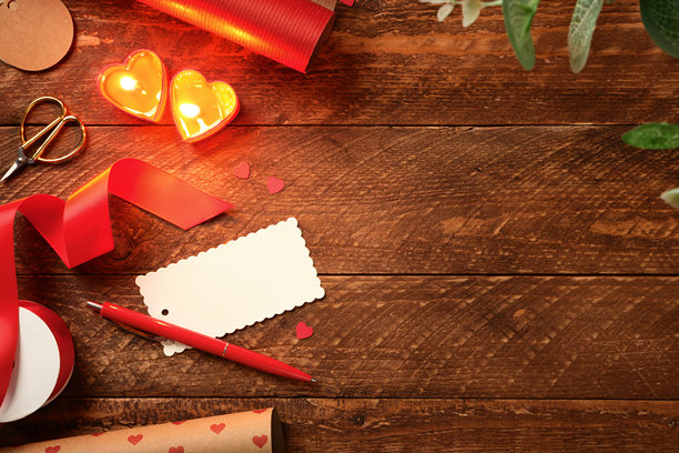 木桌上的浪漫背景，带有礼品标签、心形蜡烛、红色丝带和包装纸。留有文字空间。图片下载