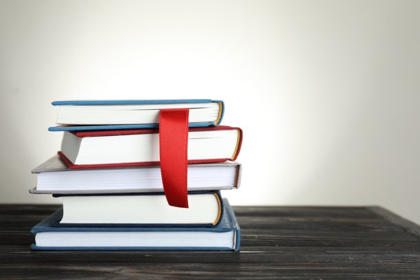 书本放在木桌上，带有红色丝带书签和其他彩色书签，背景为浅灰色。留有文字空间。图片下载