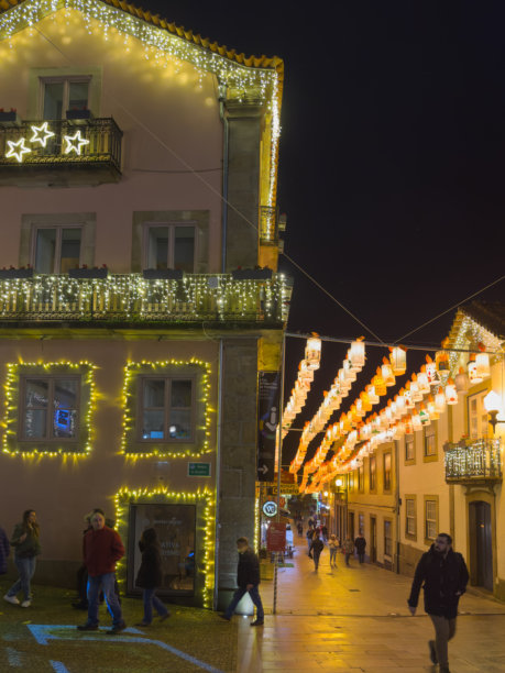 葡萄牙圣玛丽亚达费拉，2025年12月6日。舒适的圣诞灯笼点亮了葡萄牙历史悠久的街道。一张傍晚的照片，展示了圣玛丽亚达费拉一条鹅卵石街道，街道两旁挤满了人，头顶上悬挂的纸灯笼照亮了街道。图片下载