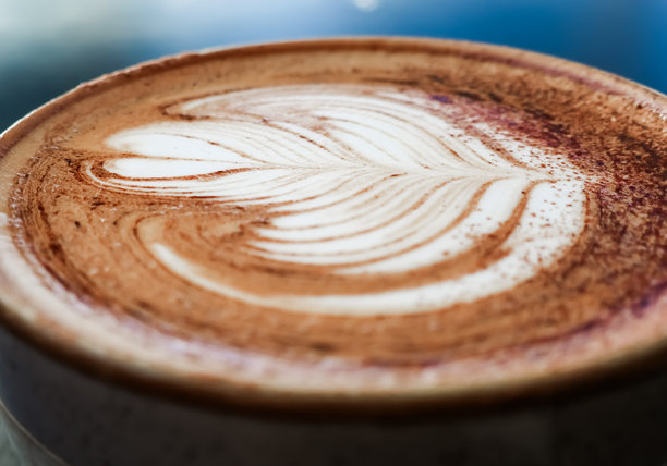 一杯咖啡，上面有细腻的奶泡和精致的拉花，形成玫瑰花图案，撒上了巧克力粉图片下载