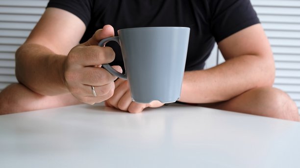 年轻男子将灰色马克杯放在桌上。早晨例行公事、早晨仪式、正念生活概念。日常行为。人与物品的接触。高质量照片图片下载