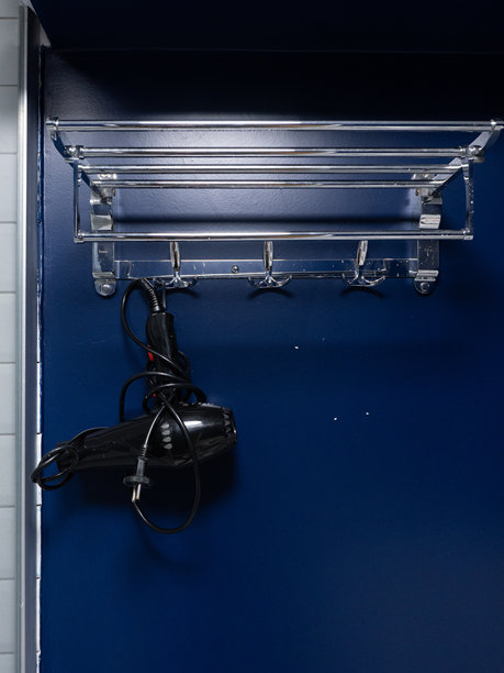 带挂钩的镀铬毛巾架，挂在蓝色墙壁上的黑色吹风机。浴室内部收纳与储物概念。竖幅照片，可供复制图片下载