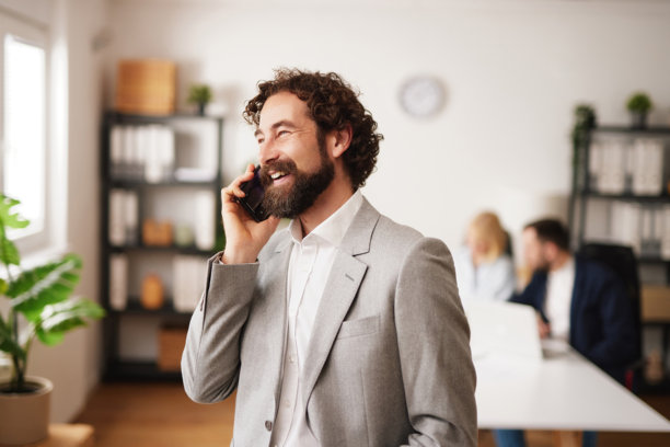 工作时间，商务人士在现代办公室空间内接听电话，同事在背景中图片下载