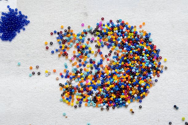 彩色种子珠子散落在白色纺织品背景上，特写镜头。手工制作的概念。图片下载