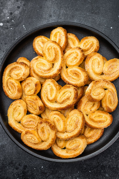 黑碗中金黄的千层酥饼干，置于深色石材背景上，留有复制空间，俯视角度拍摄的甜点烘焙食品图片下载