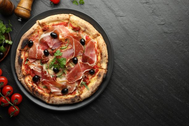 美味的比萨，配有意大利熏火腿、橄榄、番茄和欧芹，摆放在黑色桌子上，俯视角度。留有文字空间。图片下载