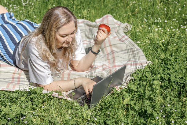 一位金发中年女性在花园的日光躺椅上使用笔记本电脑工作，绿色居家办公概念。图片下载