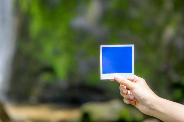 手持蓝色照片纸，背景为自然风光。用于老式相机的照片纸。图片下载