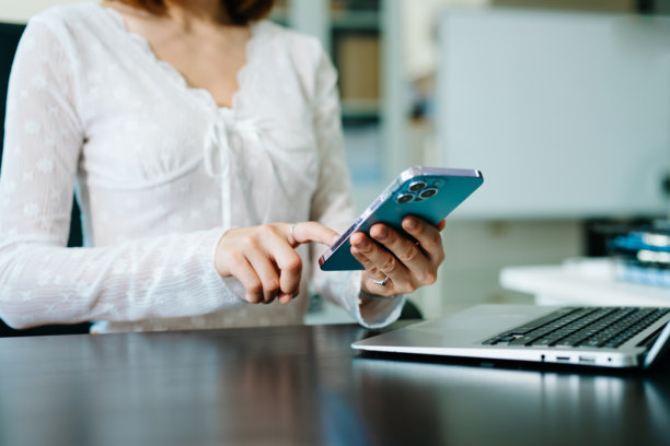 女商人在办公室的晨光中，手持手机和现代电脑，在虚拟屏幕上操作数字营销媒体，屏幕上还显示着VR图标图示。图片下载