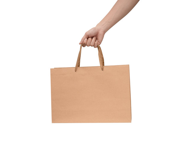 一只手拿着带提手的纸质购物袋，背景干净洁白。工作室拍摄，留有充足的空间用于文字、标志或品牌宣传。孤立在白色上，抠图。图片下载