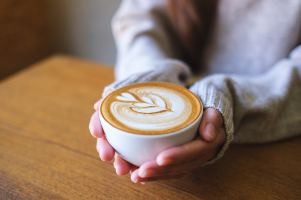 近距离拍摄一位女士手持一杯热拿铁咖啡的图片图片下载