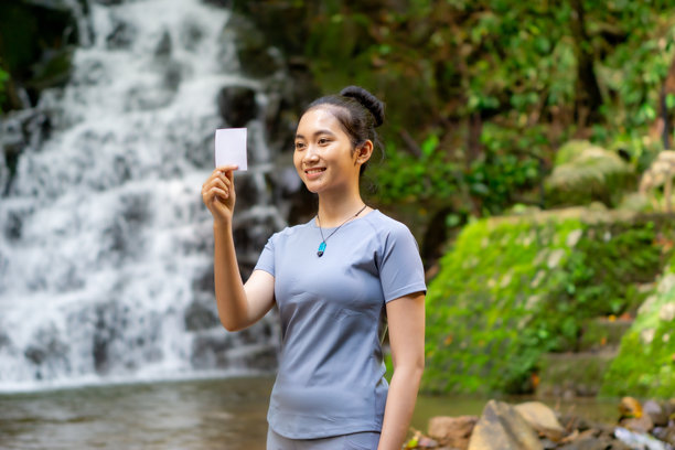 独自旅行的亚洲女性，手持带有瀑布背景的照片纸图片下载