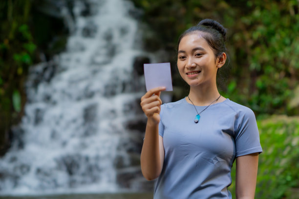 一位亚洲女子独自旅行，手持带有瀑布背景的照片纸图片下载