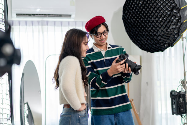 亚洲美女模特与摄影师在摄影棚工作。有吸引力的专业摄影师为广告拍摄捕捉年轻女孩的美丽照片，背景是背景板。图片下载