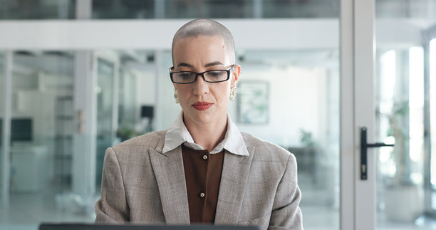一位成熟的女性在办公室使用电脑进行审查，戴着眼镜，可能是在金融公司洽谈交易。这位人士是经纪人或顾问，使用电脑进行资产管理、股票或市场研究，服务于投资机构。图片下载
