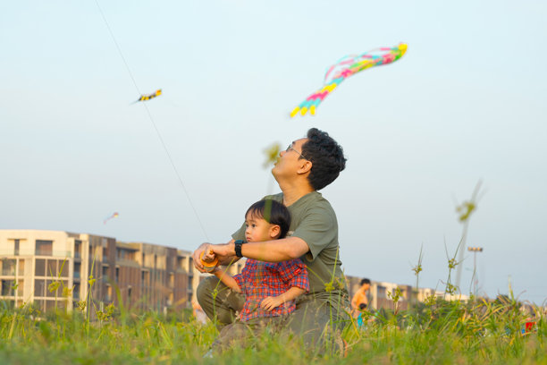 阳光明媚的下午，亚洲宝宝和爸爸在放风筝的草地上玩耍。照片素材图片下载